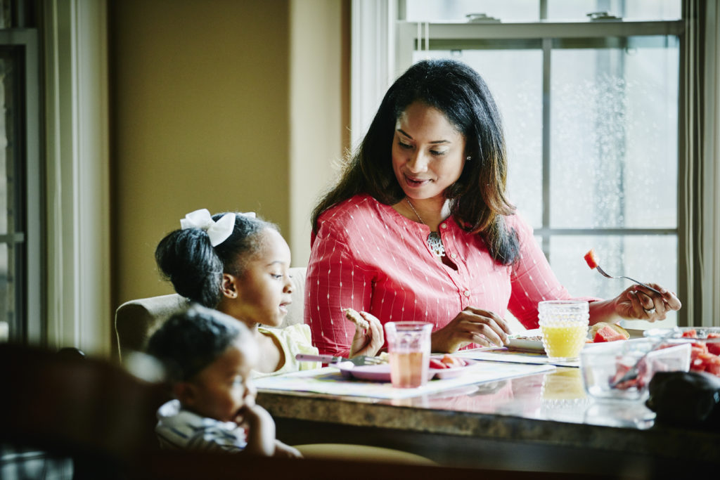 Smiling mother in discussion with young daughter during breakfast at dining room table